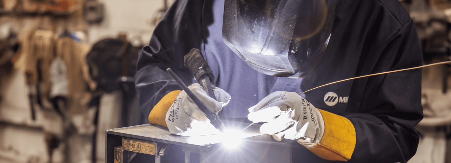 man wearing welding mask welding metal pieces together with welding tools in hand